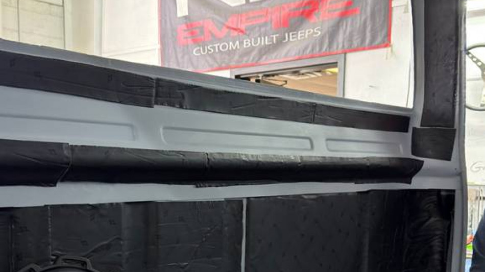 Cabin of Project Reborn-001 with Second Skin Audio sound deadening applied to roof and rear cab wall, with a subwoofer held in the foreground